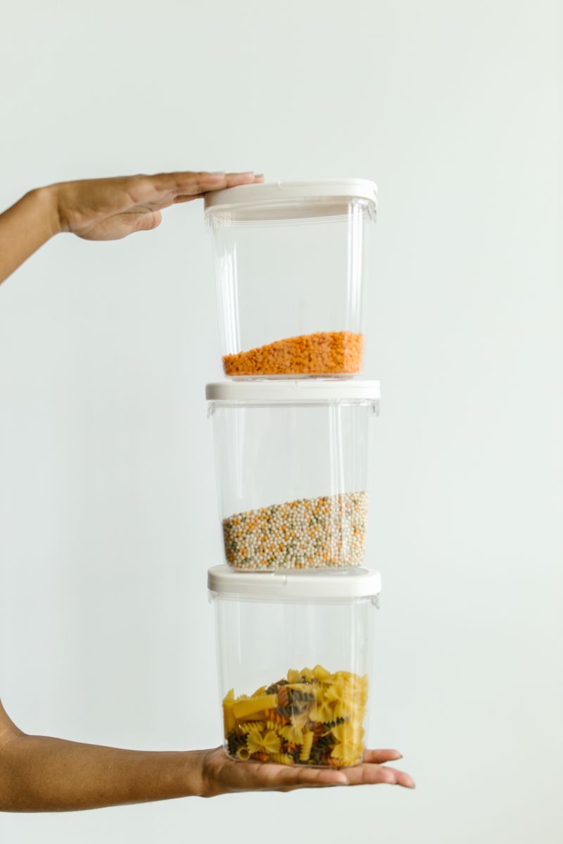 Hands holding stacked clear containers filled with dry pantry staples