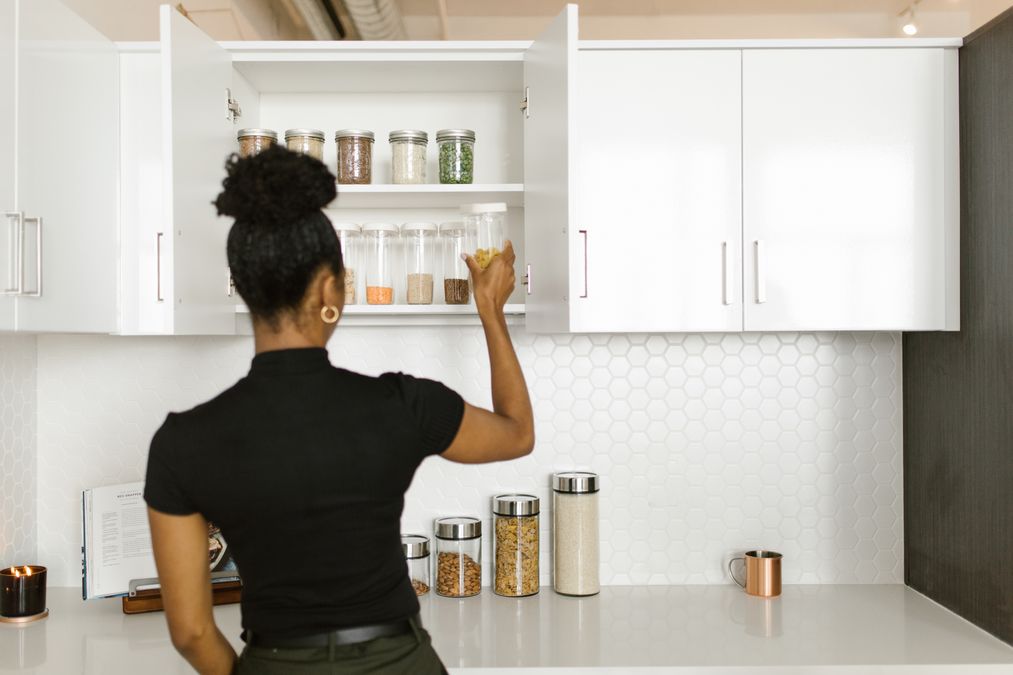Mulher organizando potes de vidro transparentes em um armário de cozinha