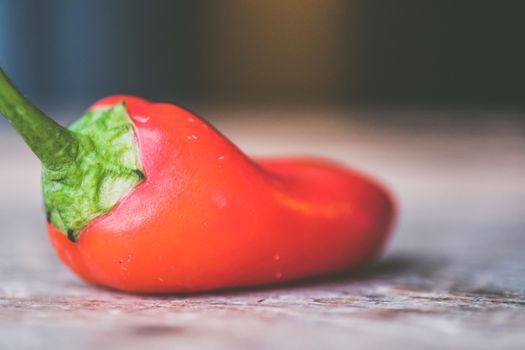 Vibrant red pepper lying on a wooden surface, showcasing freshness and organic texture.