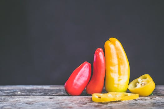 Close-up of red and yellow bell peppers on a rustic wooden table against a dark background.