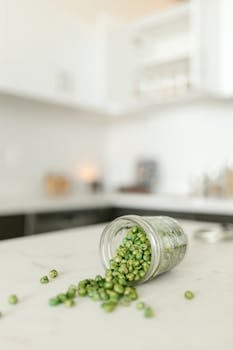 Close-up of green beans spilled from a glass jar on a marble top kitchen counter.