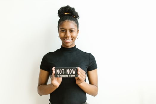 Portrait of a smiling woman with hoop earrings holding a funny sign against a white background.