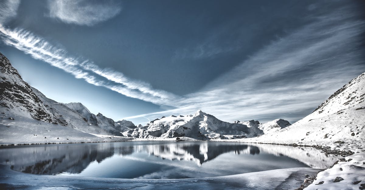 A breathtaking view of a snowy mountain lake reflecting the sky, with serene winter scenery.