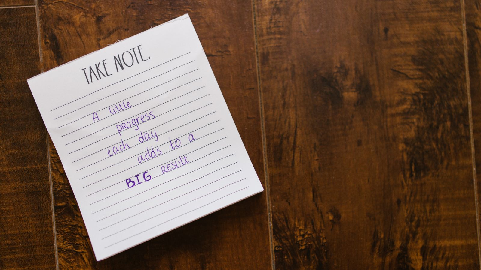 A handwritten motivational quote in an open notebook on a wooden surface