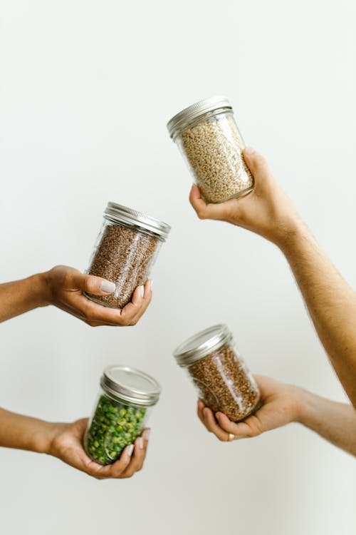 Hands of Persons Holding Glass Jars With Food Grains