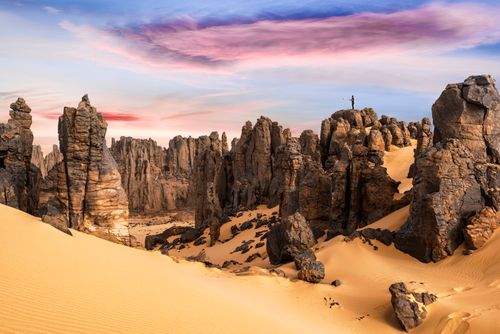 Free Stunning sunrise over the Hoggar Mountains with dramatic rock formations and a lone hiker. Stock Photo