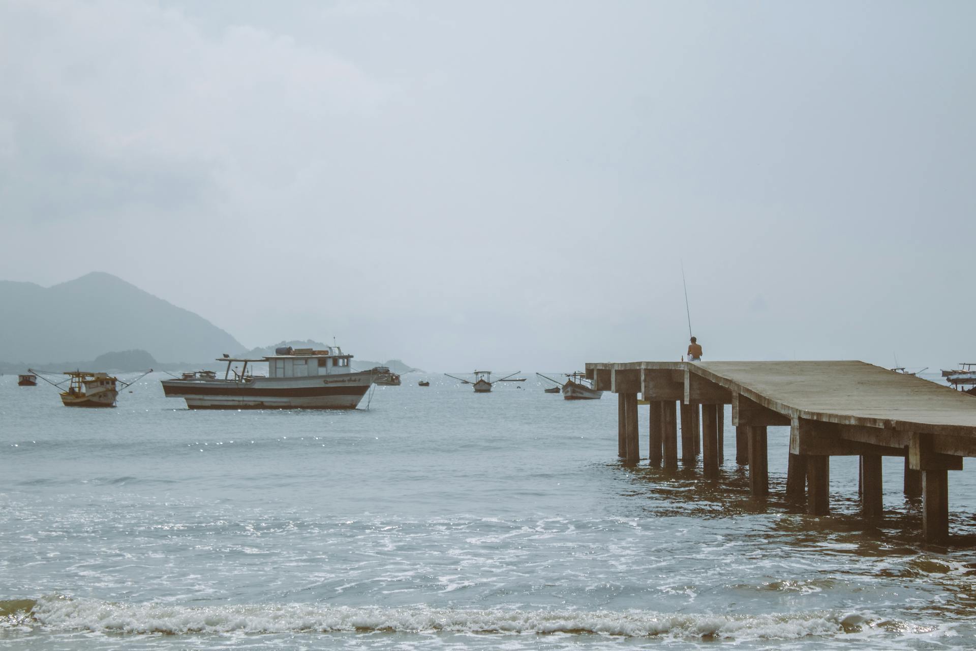 Peaceful scene of fishing boats and jetty in Guarujá, Brazil under a clear sky.