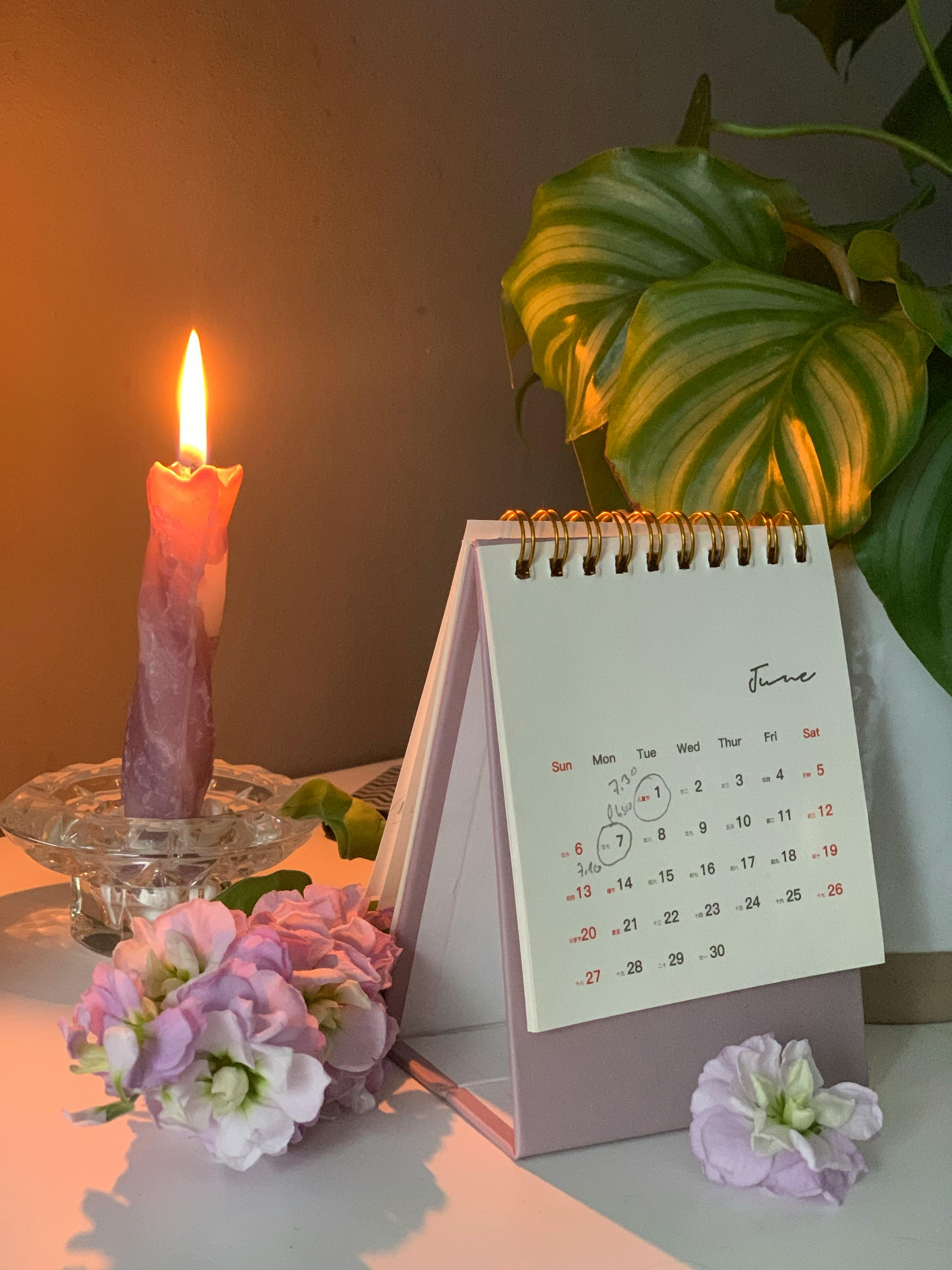 A warm, cozy desk scene with a lit candle, calendar, and flowers creating a serene ambiance.