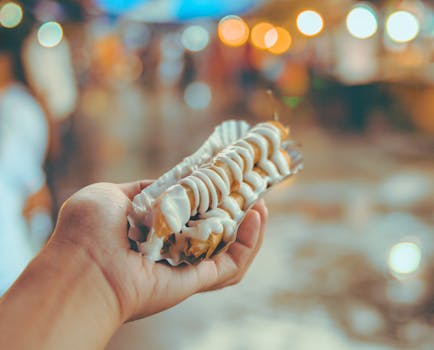 Hand holding a delicious street food dessert with creamy topping, bokeh background.