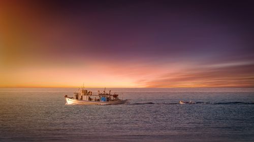 Free A serene image of a fishing boat navigating a calm sea at sunset, with colorful skies. Stock Photo