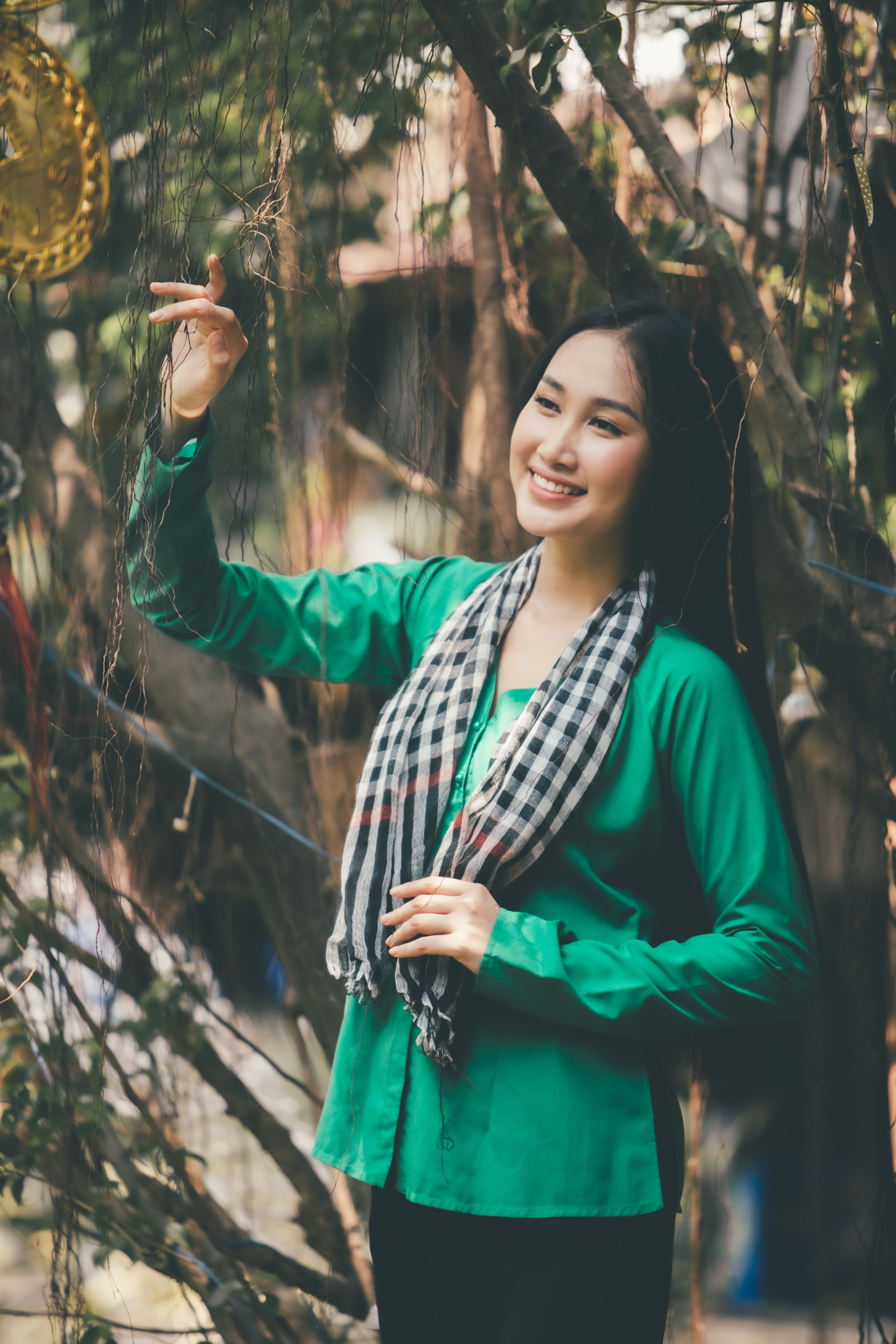A woman joyfully interacts with nature in an outdoor setting, wearing a green top and scarf.