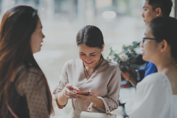 Smiling Elegant Woman Looking At Mobile Phone And People On An Event