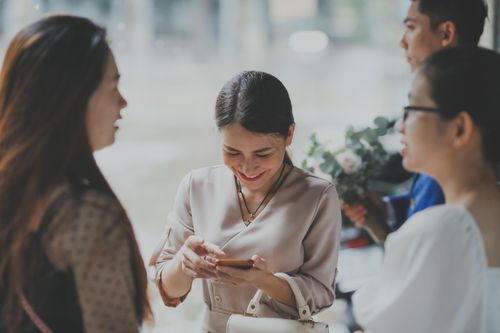 Free Women socializing and using a phone at a wedding event, creating connections with a joyful atmosphere. Stock Photo