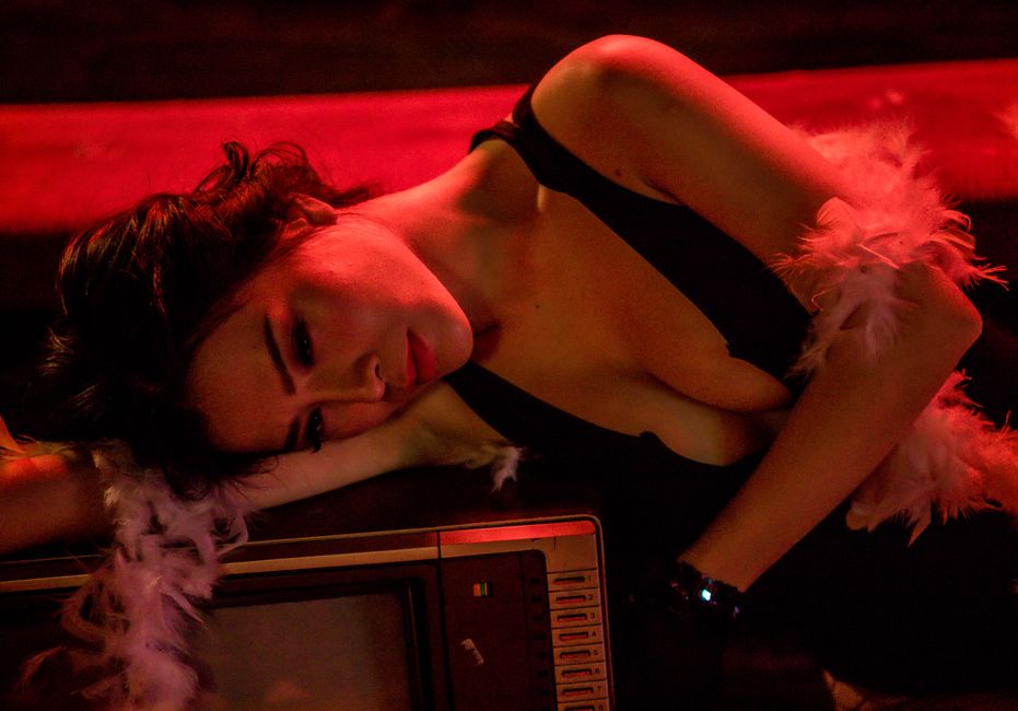A woman in a black dress lies under warm red lighting, exuding a moody and dramatic atmosphere.