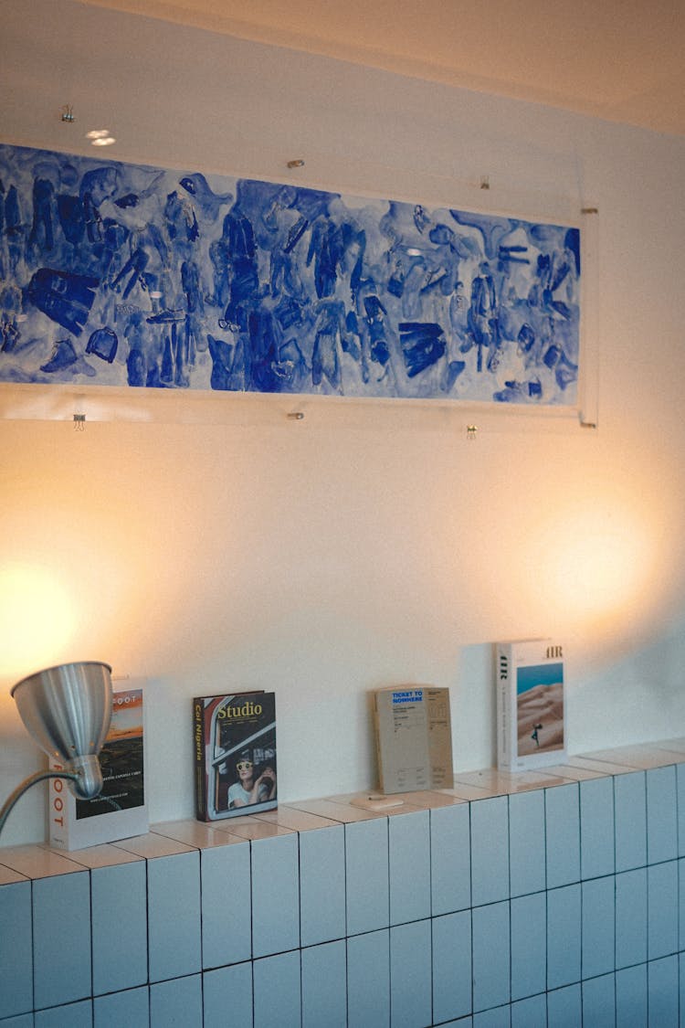 Framed Painting On White Wall Near The Tiled Shelf With Books