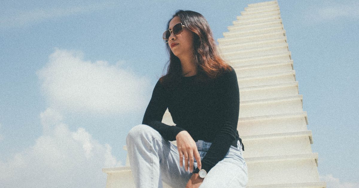 Rüyada Sonsuz Bir Merdivende Tırmanmak - Rüya Tabiri ve Anlamı - A woman in black long sleeves sits stylishly on a white staircase under a blue sky.