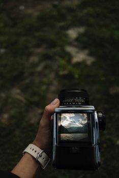 A classic vintage camera displaying a scenic mountain and lake view through its viewfinder in an outdoor setting.