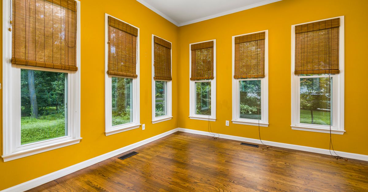 Spacious room with wooden floors, yellow walls, and large windows overlooking greenery.