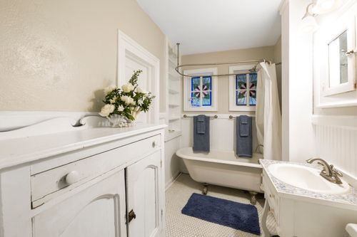 Free Vintage bathroom featuring a clawfoot tub, white furnishings, and stained glass windows enhancing the elegant ambiance. Stock Photo