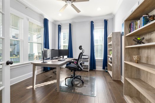 A bright modern home office featuring a desk, computer, and bookshelves with ample natural light.