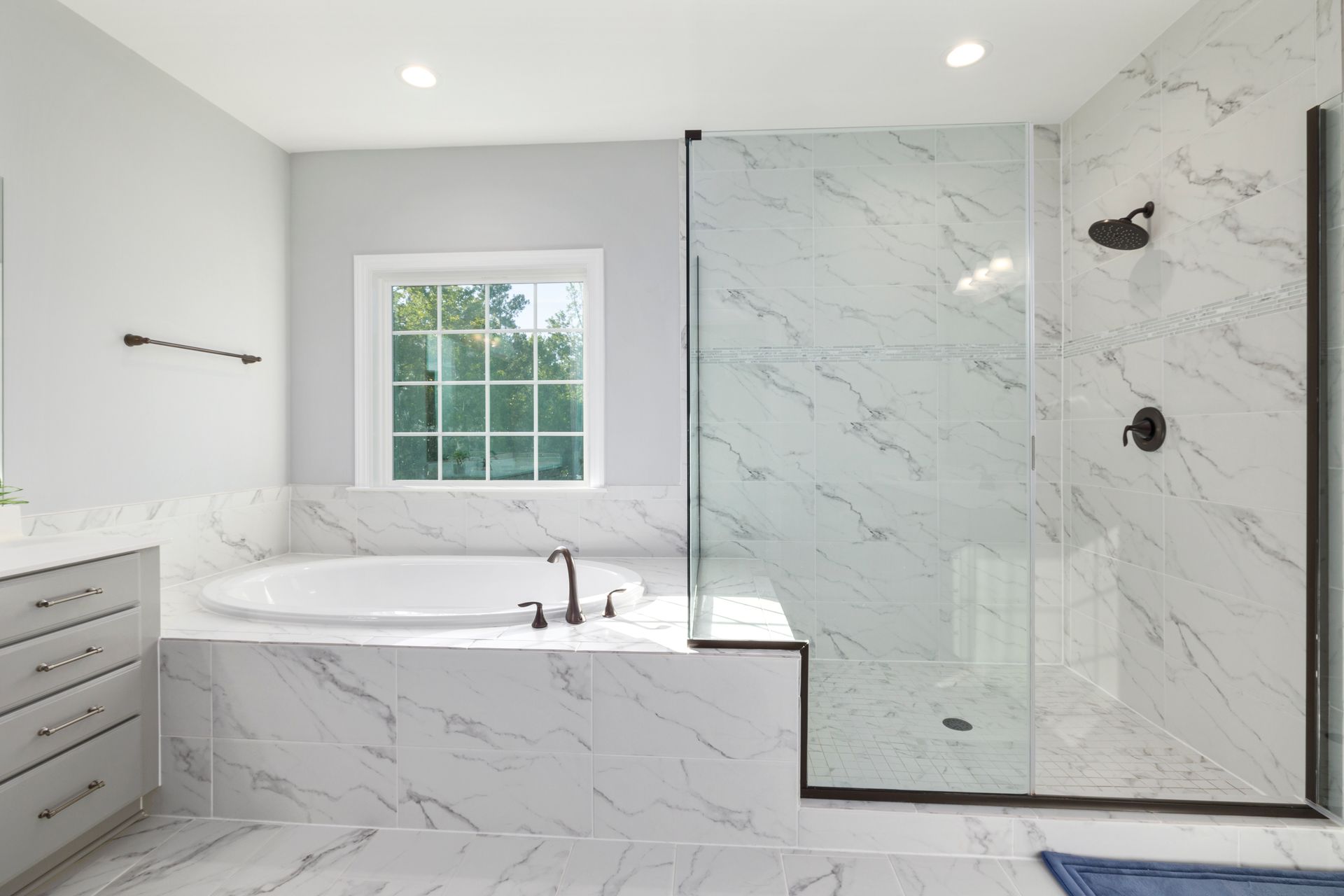 Elegant minimalist bathroom featuring a marble bathtub and glass shower with modern fixtures.
