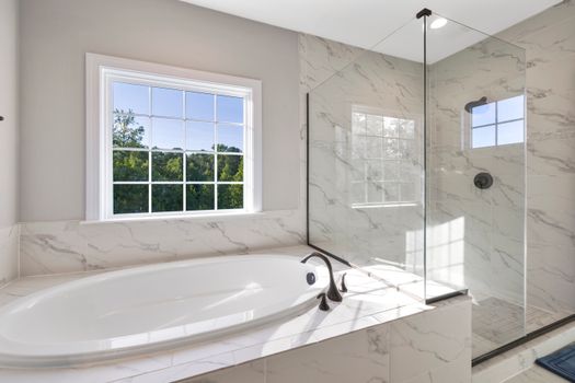 Elegant contemporary bathroom with marble finishes, featuring a sleek bathtub and glass shower.