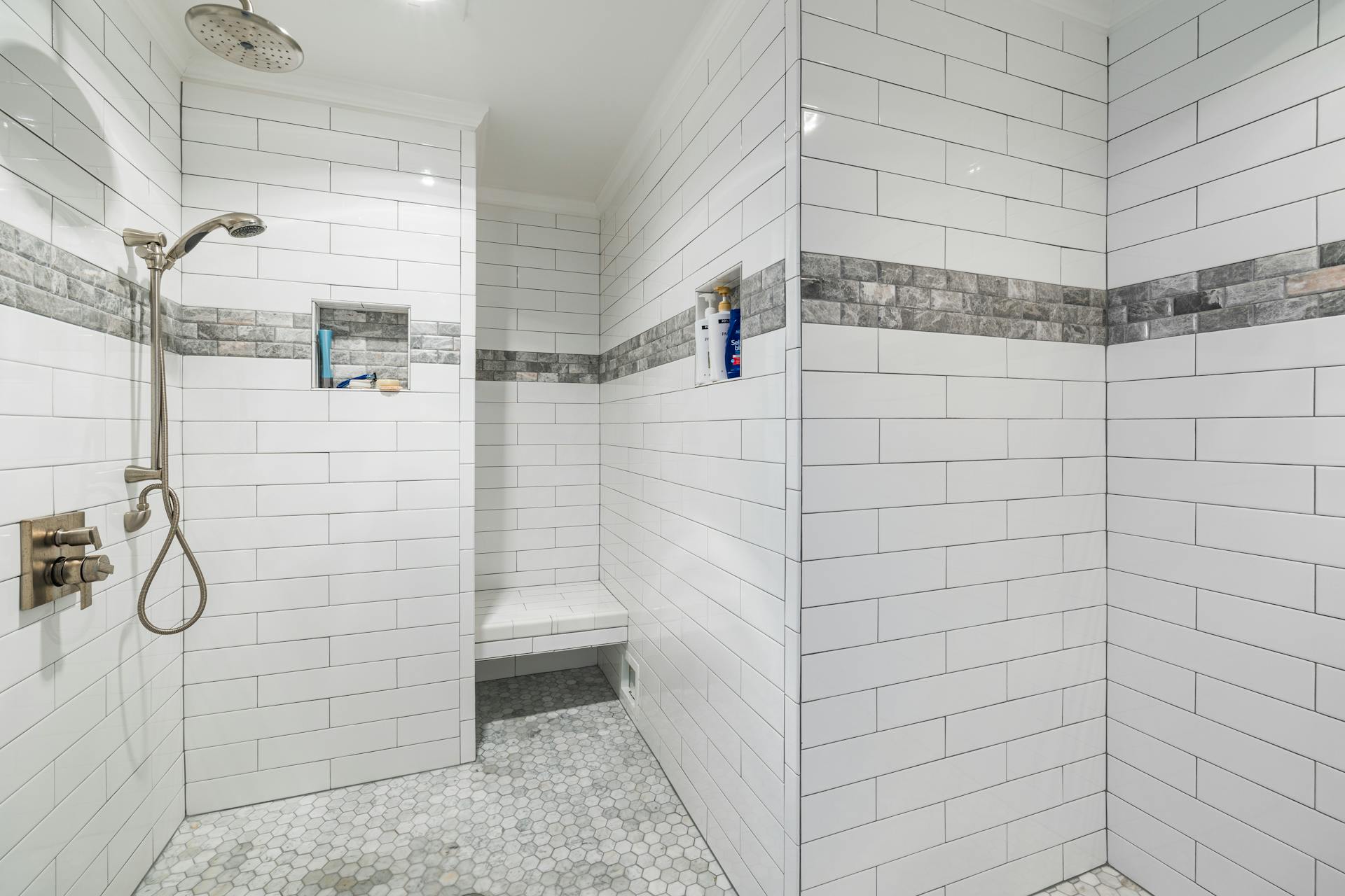 Sleek and minimalistic white tiled walk-in shower with modern fixtures and mosaic floor.