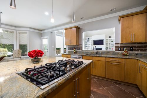 Free Spacious modern kitchen featuring granite island, gas stove, and natural lighting for a cozy interior. Stock Photo