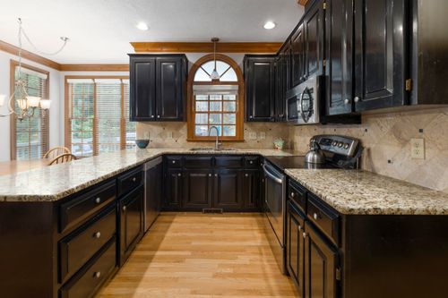 Free A modern kitchen featuring dark cabinetry, granite countertops, and hardwood floors under bright daylight. Stock Photo