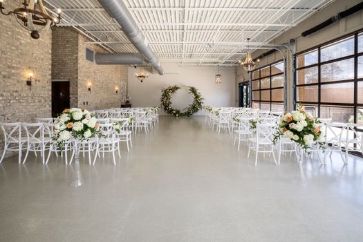A beautifully arranged indoor wedding venue featuring floral decorations and white chairs.
