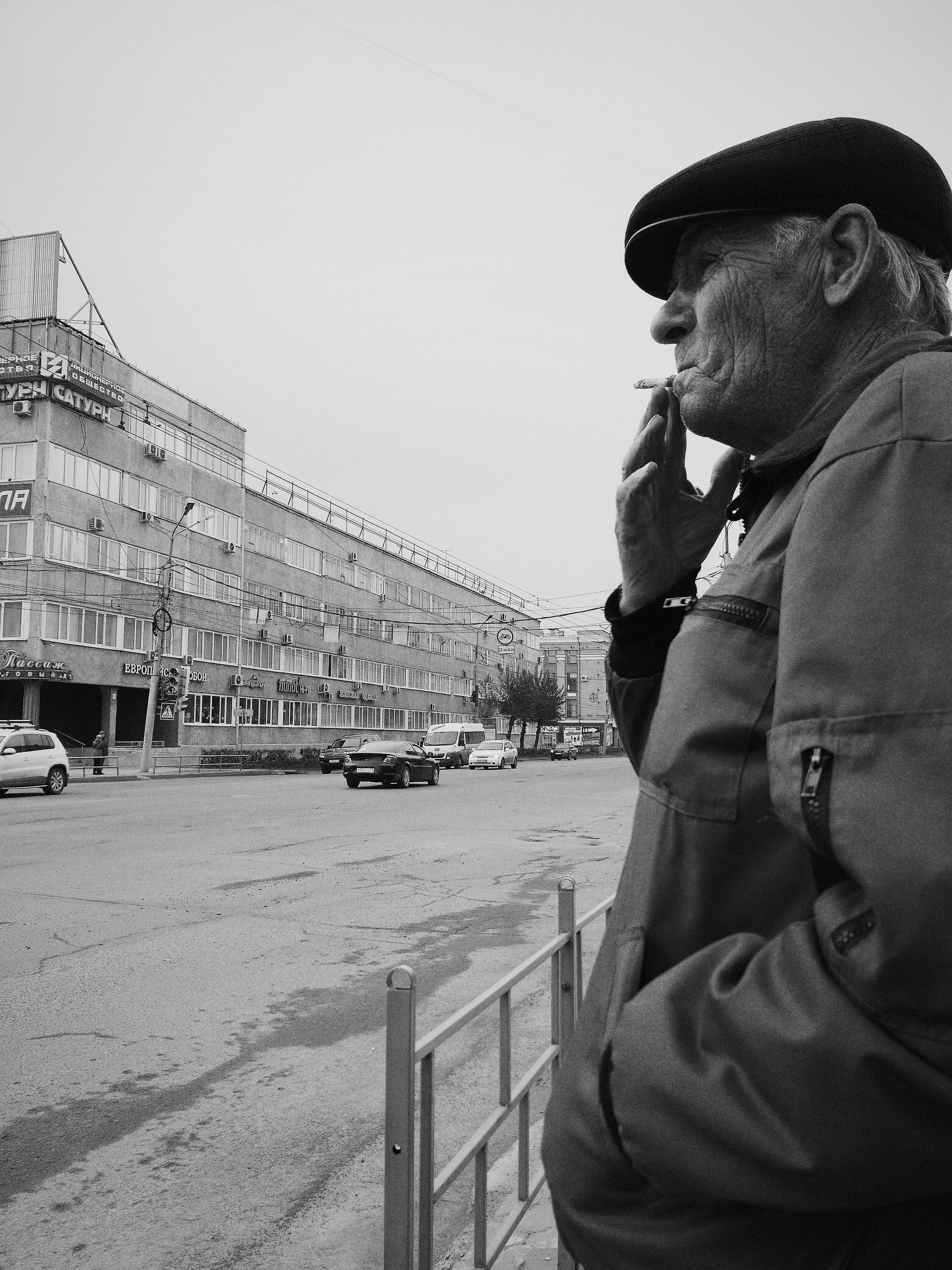 Senior man smoking on a city street in grayscale, capturing a moment of reflection and urban life.