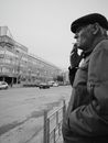 An Elderly Man with a Hat Standing on Side Street Smoking