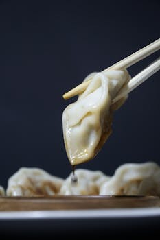 Close-up of dumplings being picked with chopsticks, dripping soy sauce, showcasing Asian cuisine.