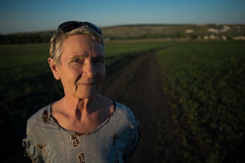 An Elderly Woman Standing on the Road Between Grass Field