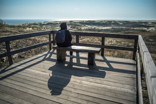 A Person in Black Hoodie Sitting on a Wooden Bench on a Viewing Deck