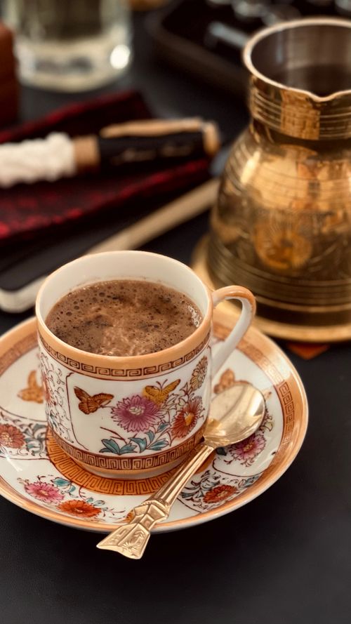 Free Rich coffee served in an ornate cup and saucer, complemented by a brass pot and spoon enhancing the cozy atmosphere. Stock Photo