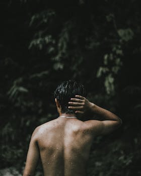 Artistic back view of a topless man in a lush forest, creating a moody ambiance.