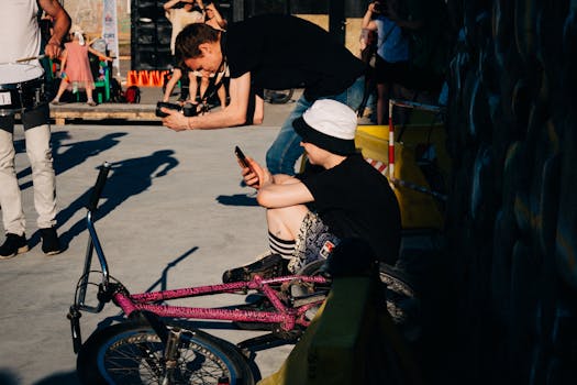 A young man in a bucket hat using a mobile phone, sitting with his bike in an urban setting.