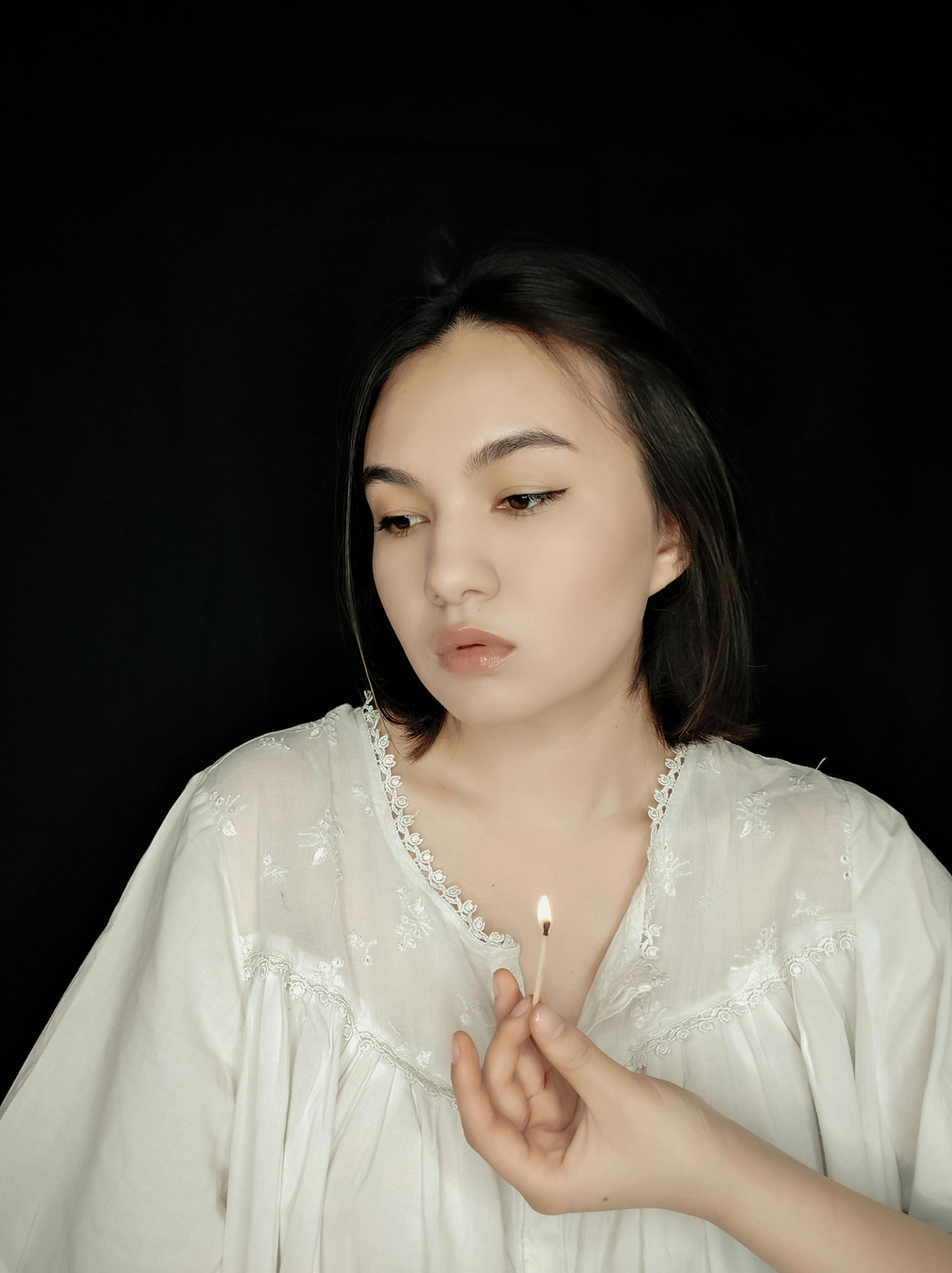 Asian woman in a white blouse holding a lit match, set against a black background