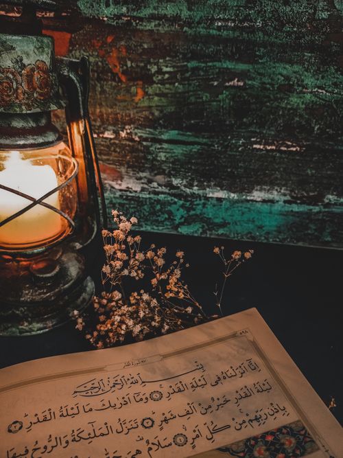 Free Vintage lantern casting warm light on dried flowers and Arabic text paper, evoking a nostalgic atmosphere. Stock Photo