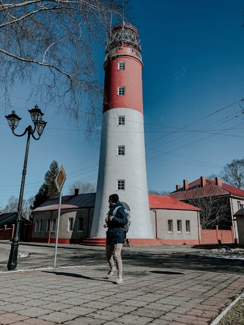 Free Man in Blue Jacket Standing near Red and White Lighthouse Stock Photo