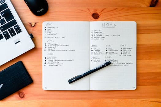 Flat lay of an open notebook with handwritten notes, laptop, and pen on a wooden desk.