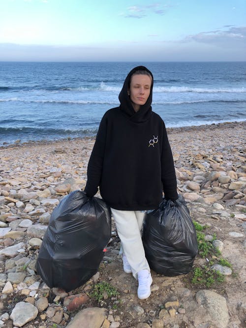 Free A Person Carrying Garbage Bags on Rocky Seashore Stock Photo