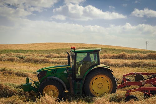 Free Man Driving a Tractor on Hay Field Stock Photo