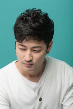 Portrait of a young Asian man in a white shirt with a stylish hairstyle on a teal background.