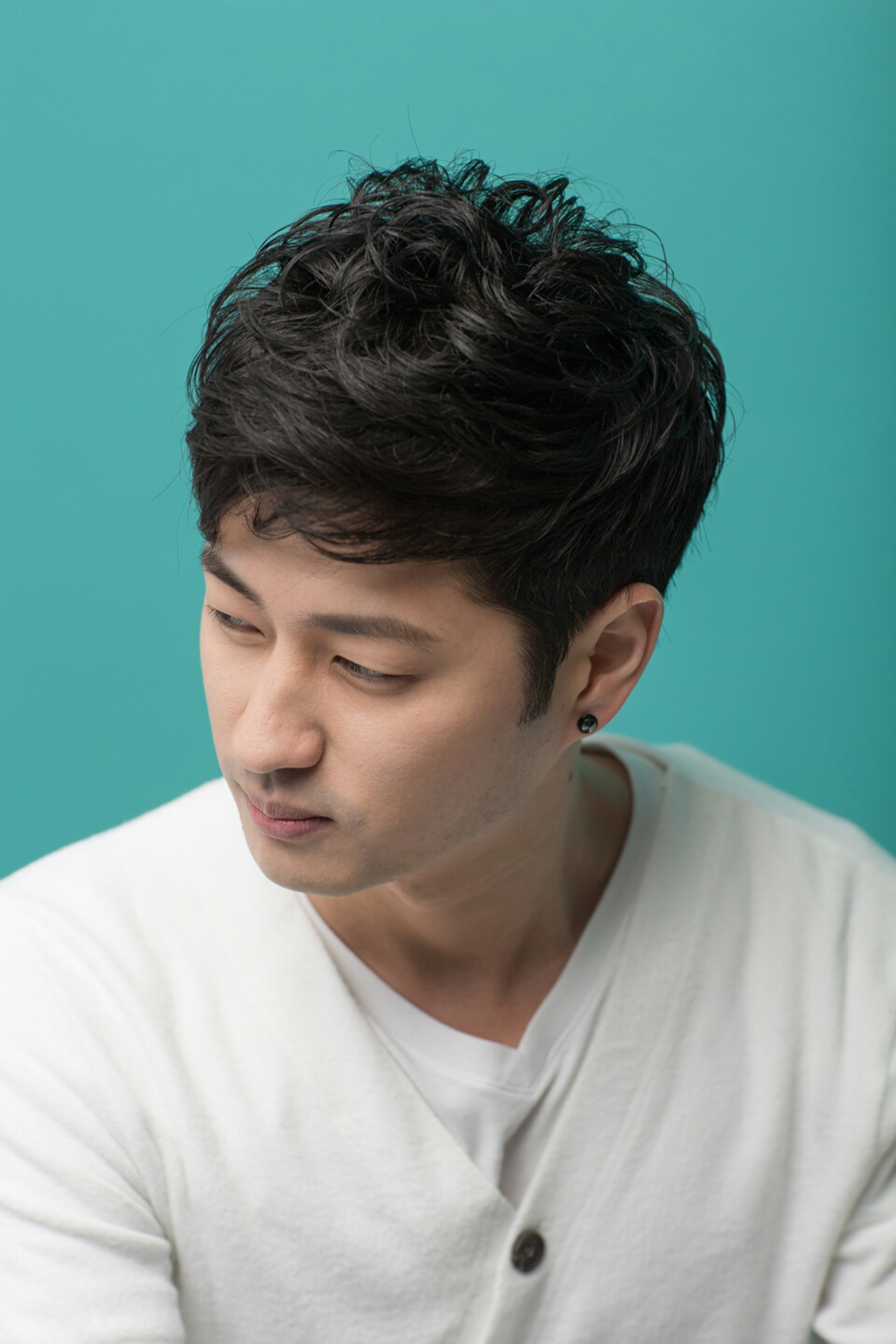 Close-up of a young man in a white sweater looking sideways against a teal background.
