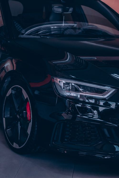 Free Close-up of a glossy black luxury car with prominent headlights reflecting light. Stock Photo
