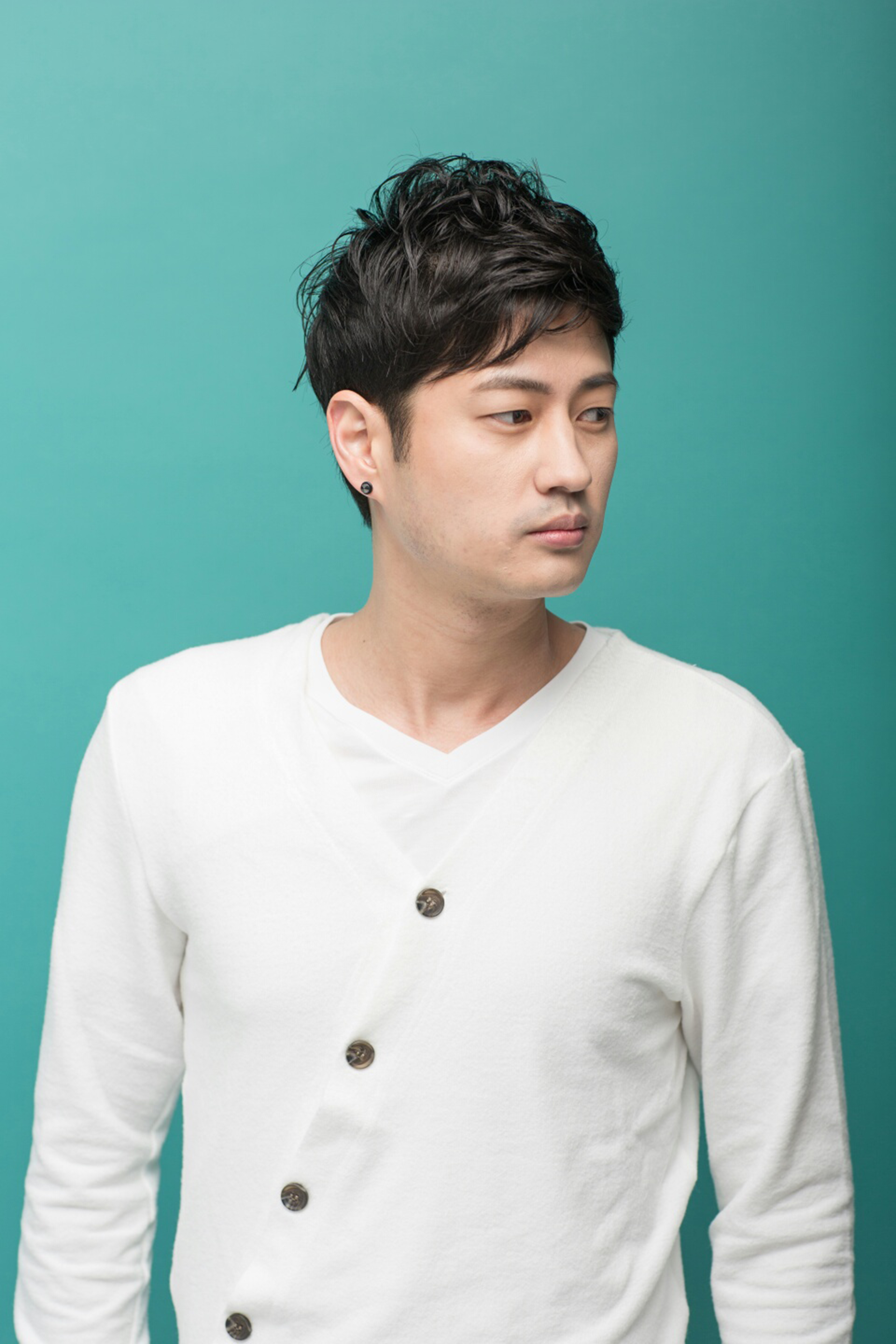 Portrait of a stylish Asian man in a white sweater against a teal background.
