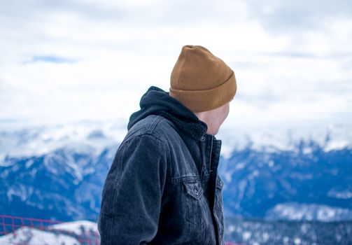 A man in winter clothing admires a snowcapped mountain range on a clear day.