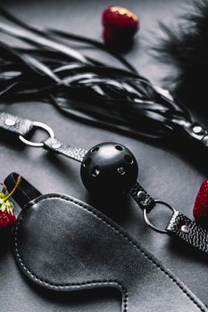 Close-up of BDSM gear including blindfolds and ball gags, with red strawberries.